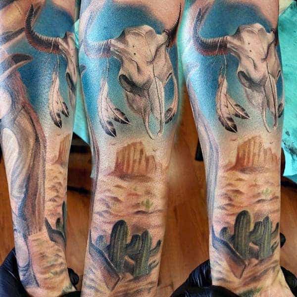 Colorful desert-themed tattoo with cattle skull and feathers on an arm
