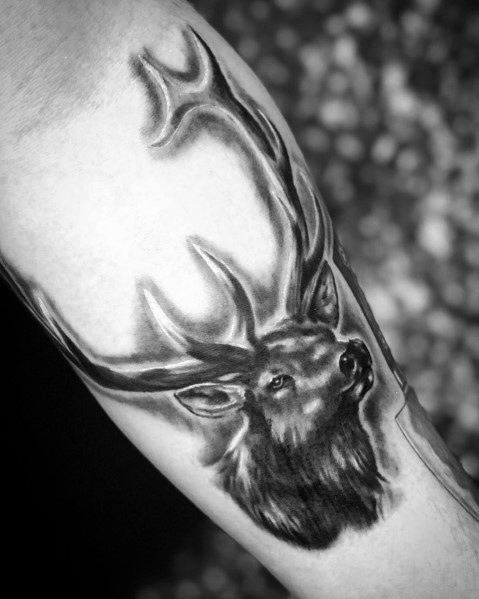 Realistic black and grey elk tattoo on the bicep, featuring intricate shading, bold antlers, and lifelike fur details for a striking design.