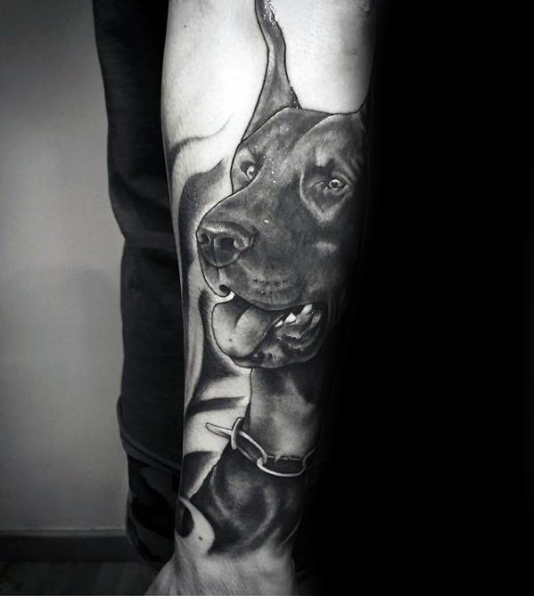 Realistic black and grey Doberman tattoo with a happy, alert expression, detailed fur, and soft background shading for depth.