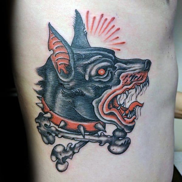 Neo-traditional Doberman tattoo with exaggerated features, a spiked collar and bones, red highlights, and a fierce open-jaw snarl.