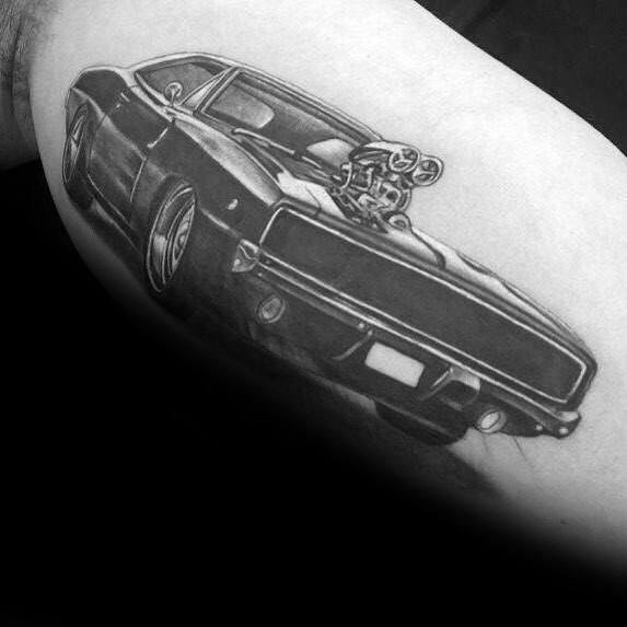 Black and grey Dodge Charger tattoo with a supercharged engine, detailed shading, and a bold muscle car design on the arm.