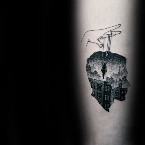 Blackwork tattoo of a hand controlling a suspended figure above a cityscape shaped like a head, symbolizing control, isolation, and introspection.