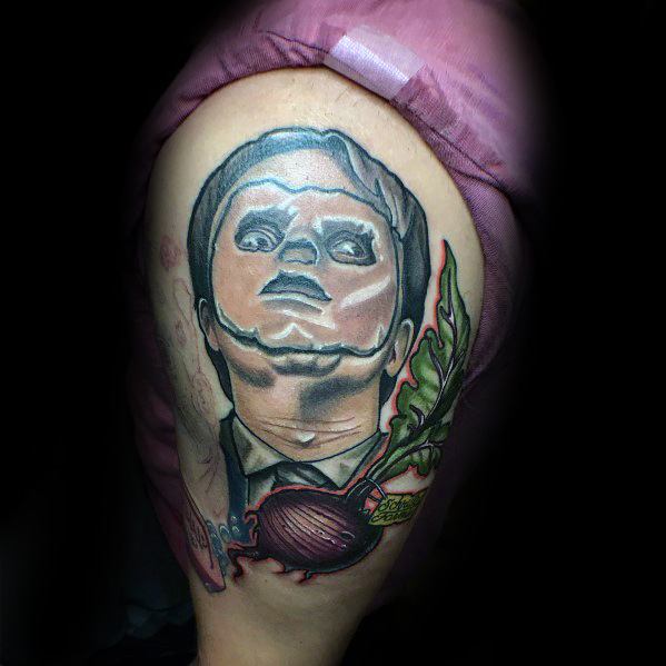 Tattoo of Dwight Schrute with a puppet-like face, featuring bold shading, a detailed beet with leaves, and surreal elements on the upper arm.