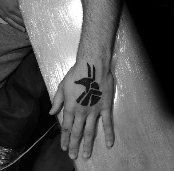 A hand with a black tattoo of an abstract bird design on the back
