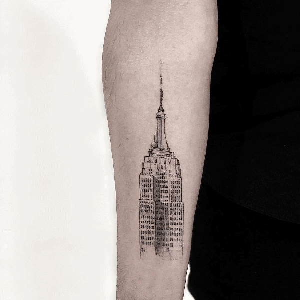 Fine-line Empire State Building tattoo with delicate detailing, neatly placed on a man's forearm.
