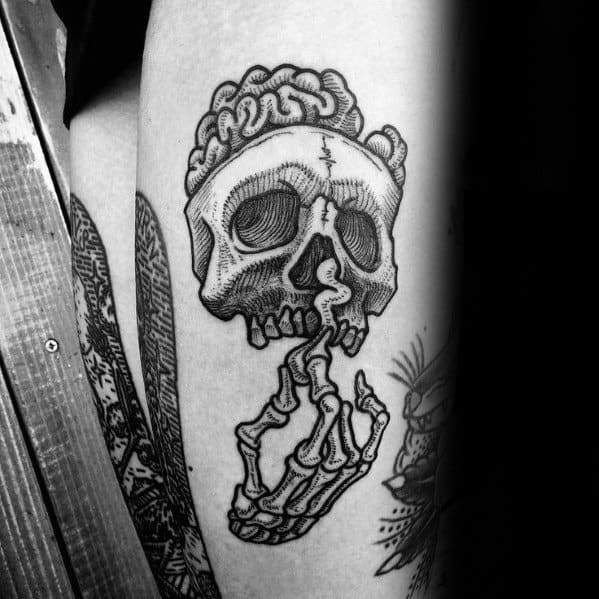 Tattoo of a skull with an exposed brain, being held up by a skeletal hand gripping its jaw in a haunting and surreal pose.