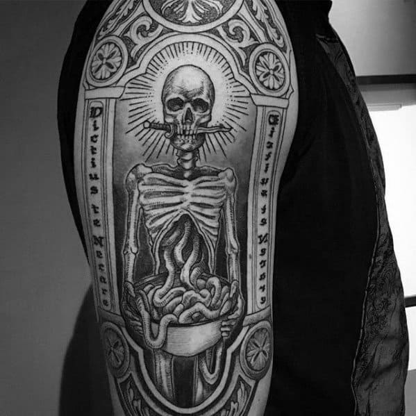 Tattoo of a radiant skeleton holding a bowl of entrails, framed in an ornate design with Latin script and symbolic gothic elements.