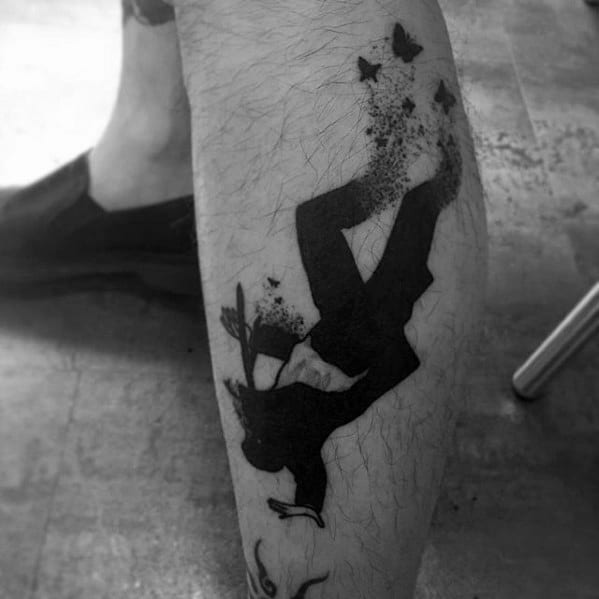Silhouette tattoo of a falling man in a suit dissolving into butterflies, symbolizing transformation or release, inked on the calf.