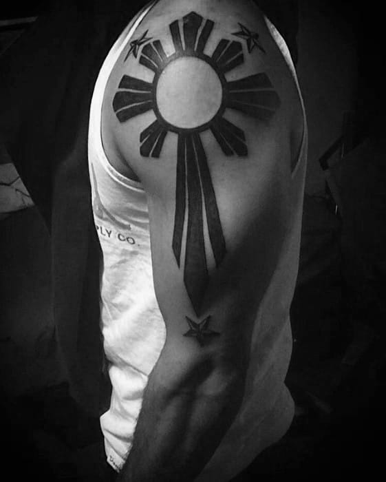 Filipino sun tattoo on the upper arm with long central rays forming a cross-like shape, surrounded by three bold stars in a minimalist style.