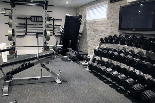 Cozy home gym with weight racks, a bench press, treadmill, and flat-screen TV on stone-paneling walls
