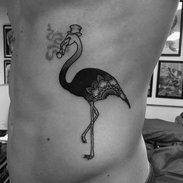 Whimsical blackwork flamingo tattoo featuring a top hat, monocle, and pipe, with mandala-style detail on the body for a quirky touch.