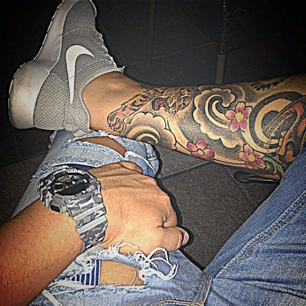 Person wearing a watch, jeans, and sneakers with a tattooed leg