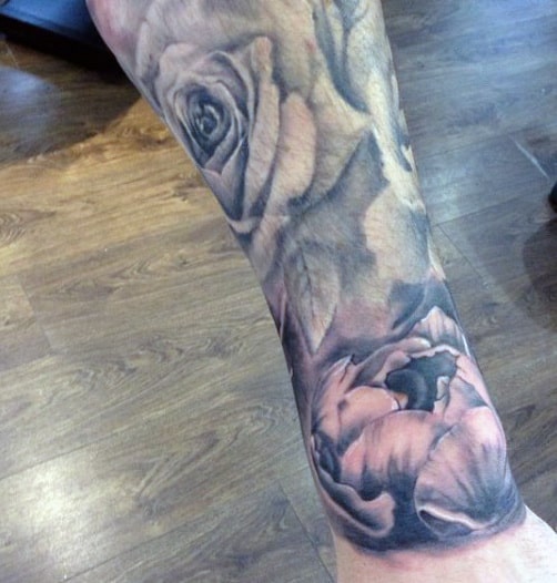 Close-up of a forearm tattoo featuring detailed roses and leaves in grayscale
