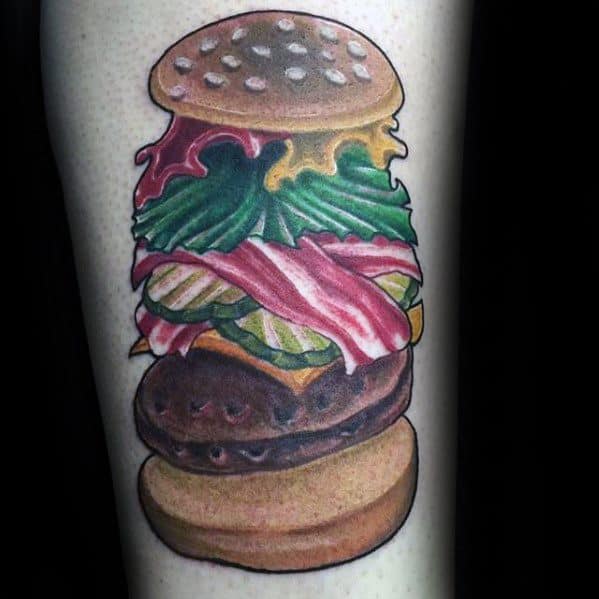 Tattoo of a cheeseburger with layers of lettuce, bacon, cheese, and beef patty on a person's skin