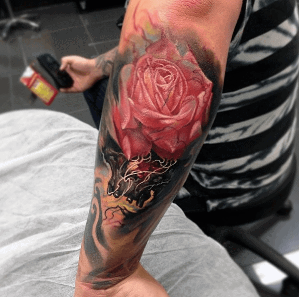 A detailed arm tattoo featuring a red rose and a dark, swirling background