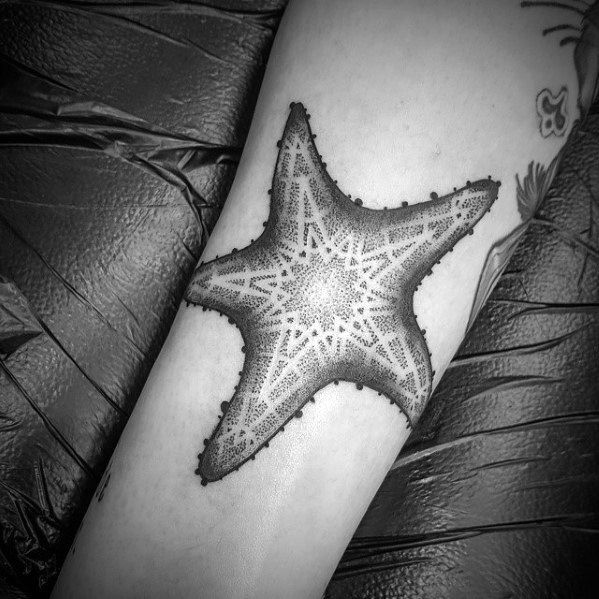 Dotwork starfish tattoo with symmetrical geometric patterns and subtle shading, centered on the forearm for a clean, bold look.