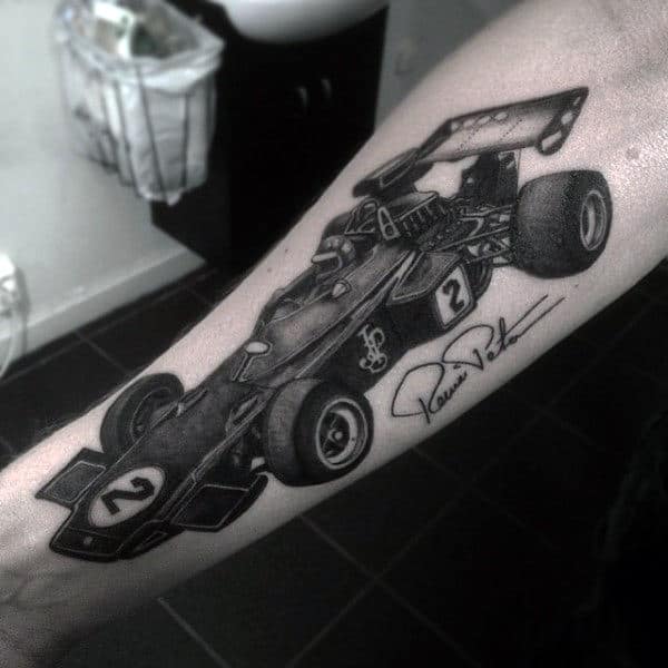 Forearm tattoo of a detailed vintage formula race car with a number 2 and a signature below set in a grayscale tone