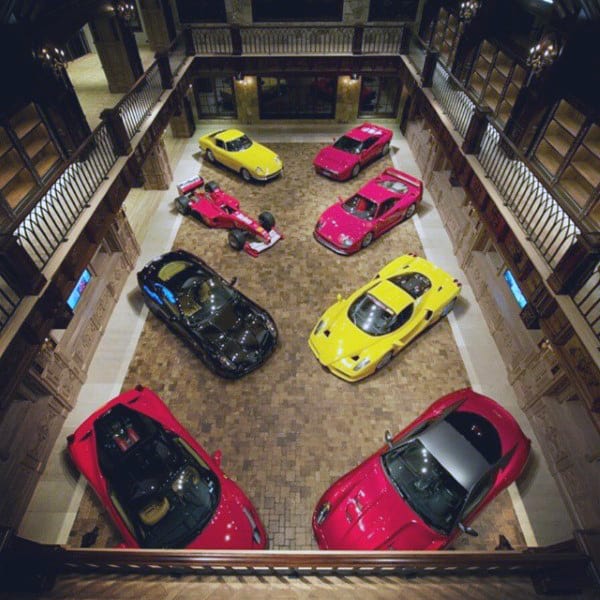 A stunning multi-level garage featuring luxury cars and race vehicles, set on a beautiful brick floor surrounded by elegant railings.