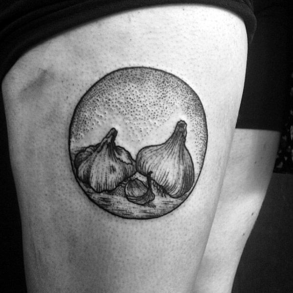 Black and grey garlic tattoo with fine dotwork shading, featuring a circular frame for a detailed and artistic botanical design on the thigh.