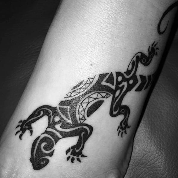 Bold black tribal gecko tattoo on foot with stylized shapes, curved lines, and sharp geometric accents.