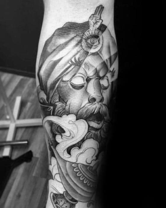 Intricate black and gray tattoo of a mystical figure with a turban, a third eye, with a genie lamp, clouds, and intricate details on an arm