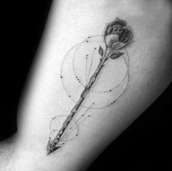 Geometric arrow tattoo with a shaded rose as the arrowhead, accented by dotted circles and fine detailing on the forearm.