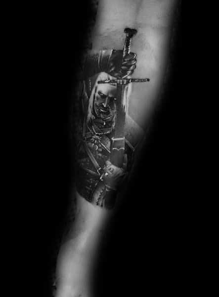 Geralt tattoo in black and gray realism, featuring him gripping a sword with an intense battle-ready expression and detailed armor shading.