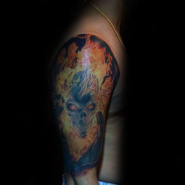 Ghost Rider upper arm tattoo with a dark flaming skull, glowing red eyes, and vibrant fire surrounding the head in an intense design.