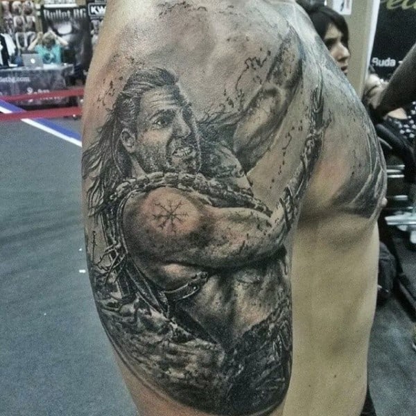 Detailed tattoo of a gladiator warrior on a muscular bicep displayed against a gym background