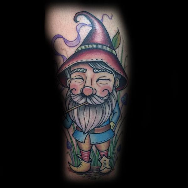 Tattoo of a cheerful gnome with a large, curved hat, bushy beard, and rosy cheeks, smoking a pipe while standing among grass and flowers.