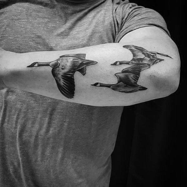 Realistic black and gray tattoo of two geese in flight, inked on the forearm with detailed shading and fine linework to capture movement.