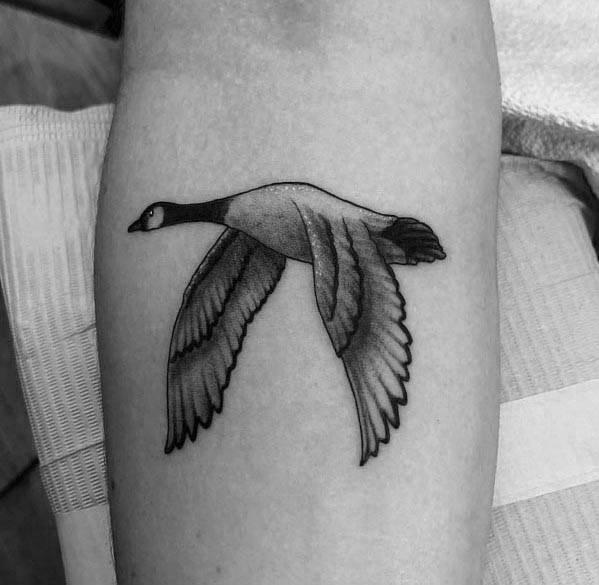 Black and gray tattoo of a flying goose, inked on the forearm with fine linework and shading for a realistic yet minimalist look.