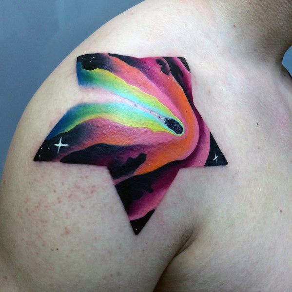 Star-shaped tattoo featuring a vibrant cosmic scene with a rainbow-colored comet streaking through a galaxy of pink, orange, and black hues.