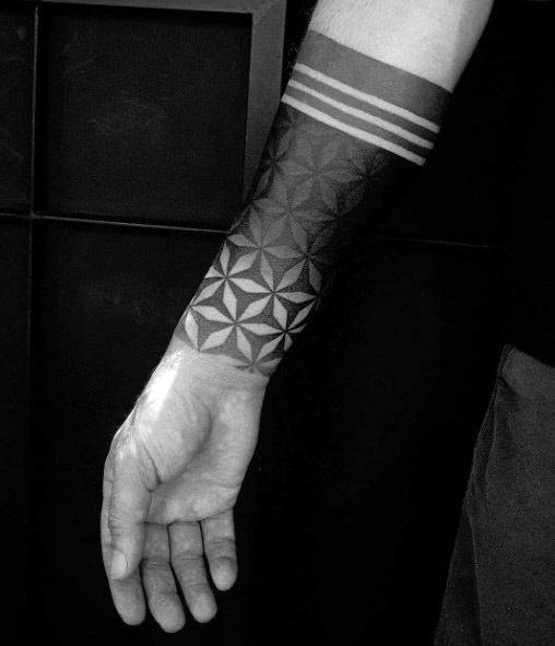 Bold blackwork forearm tattoo featuring a geometric flower of life pattern that fades into solid black bands and three parallel stripes.