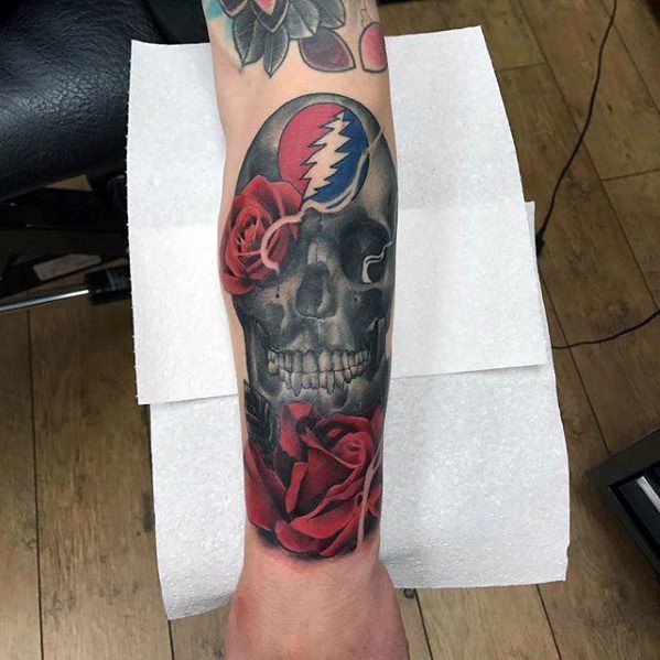 Realistic skull tattoo with red roses and the Grateful Dead lightning bolt skull logo at the top, covering the forearm.