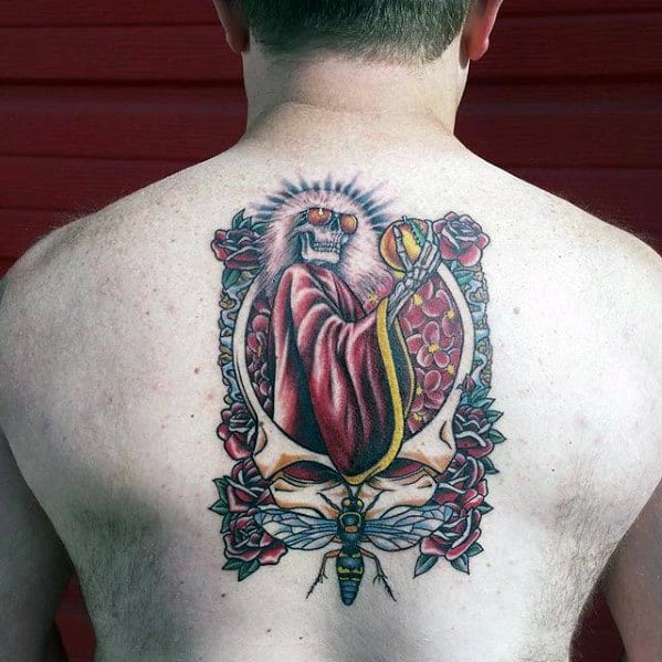Grateful Dead back tattoo of a cloaked skeleton with glowing eyes, framed by roses and skulls, featuring vibrant red and gold tones.