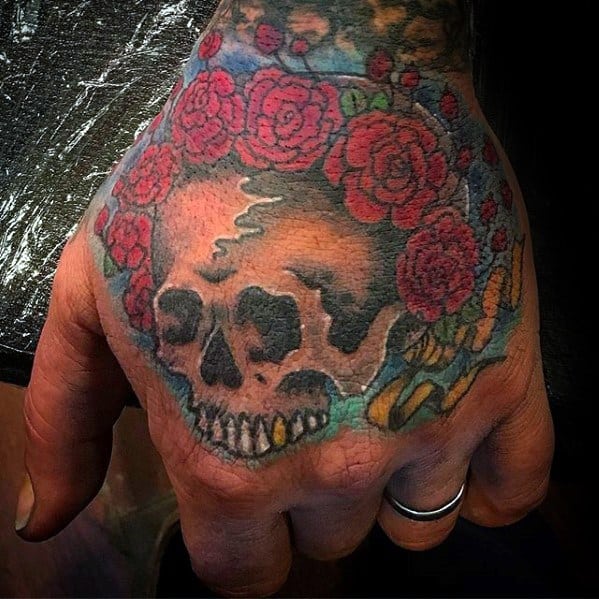 Grateful Dead skull and roses tattoo on the hand, with rich red flowers and soft shading for a worn, vintage look.