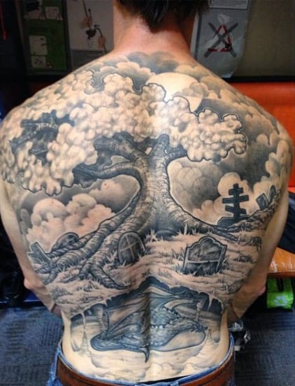 A detailed tree and graveyard landscape tattoo covering a person's entire back