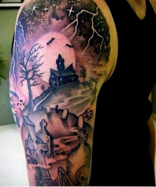Arm tattoo of a haunted house with a graveyard, leafless trees, bats, and lightning