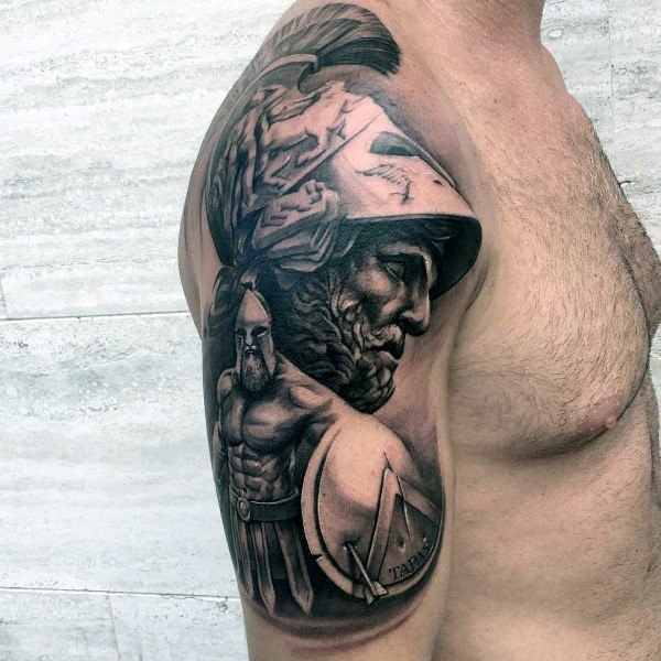 Realistic upper arm tattoo of two Spartan warriors, one in full armor with a detailed helmet and plume, and the other with a round shield.