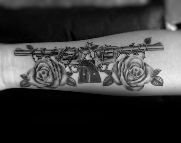 Black and grey forearm tattoo with two roses, a gun barrel wrapped in barbed wire, and a lock in the center symbolizing contrast.