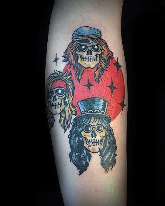 Colorful tattoo of three skulls styled as Guns N' Roses members with bandanas, hats, and hair, set against a red starry background.