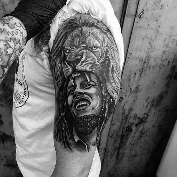 Black and gray upper arm tattoo of Bob Marley smiling with a majestic lion above his head, symbolizing strength and Rastafarian pride.