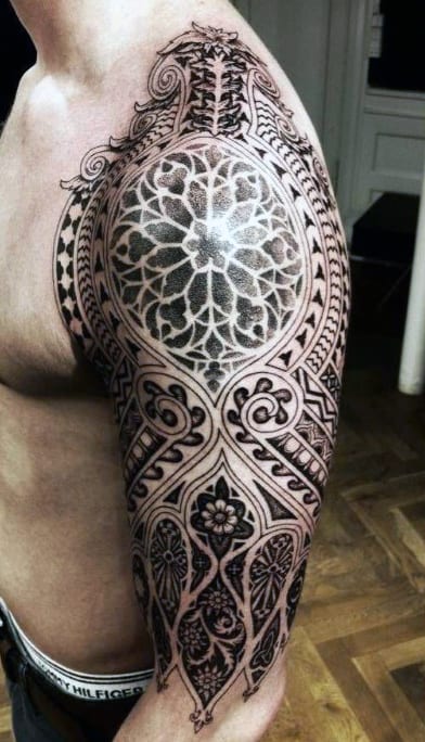 Intricate black tattoo with geometric and floral designs covering a man's upper arm