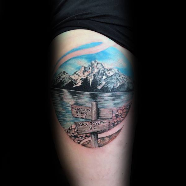 A tattoo of a scenic mountain lake with a wooden trail sign in the foreground, featuring names and a date, symbolizing adventure.