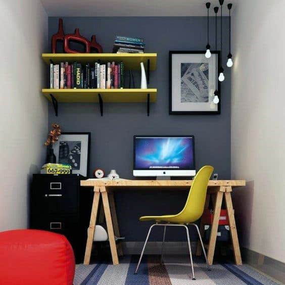 Compact workspace with a wooden desk, computer, yellow chair, shelves, and hanging lights in a cozy room