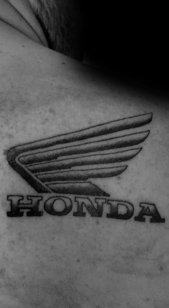 Black Honda wing logo tattoo on a man's shoulder, featuring bold lettering and detailed shading for a classic and powerful look.