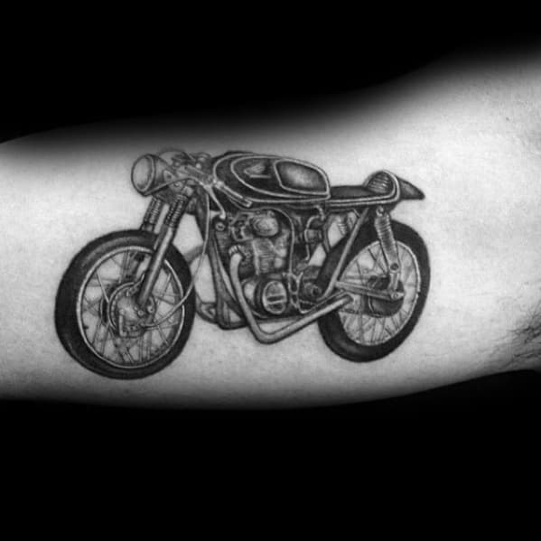 Realistic Honda café racer tattoo on a man's arm, featuring intricate details and bold shading for a vintage motorcycle look.