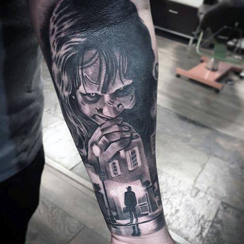 Black and grey tattoo featuring Regan from *The Exorcist* with eerie eyes, looming over the iconic scene of the priest outside the house.