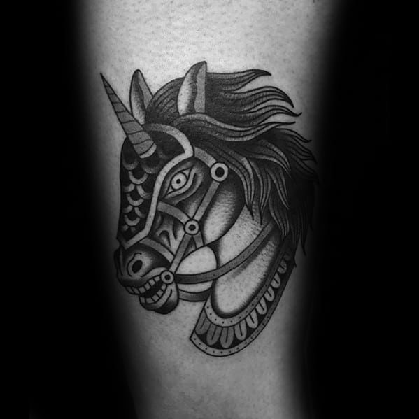 Blackwork tattoo of a fierce, stylized unicorn head with armor-like detailing and flowing mane, placed on the lower leg